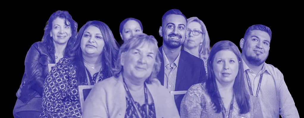 A group of diverse attendees engaging attentively in a presentation or event. They display various expressions, including smiles and focused looks, as they listen to a speaker. The background is dark, highlighting the individuals and creating a professional yet relaxed atmosphere.