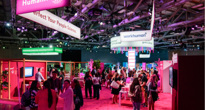 A vibrant scene from the Workhuman conference showcases attendees engaged in conversation beneath large colorful banners with text such as 